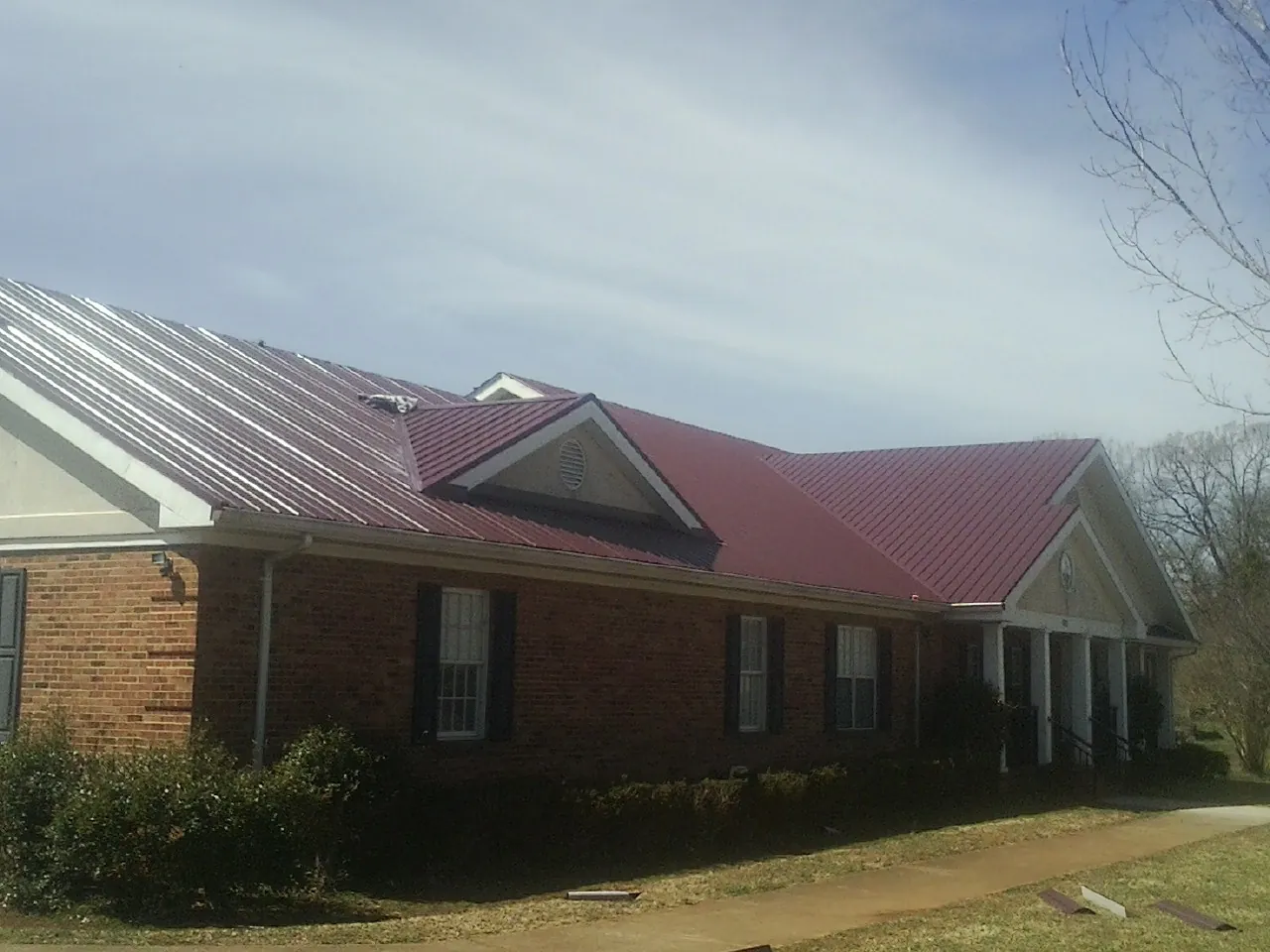 Red metal roof with gabled entries on a long brick building, from a Hail Damage Roof Repair job in Aubrey