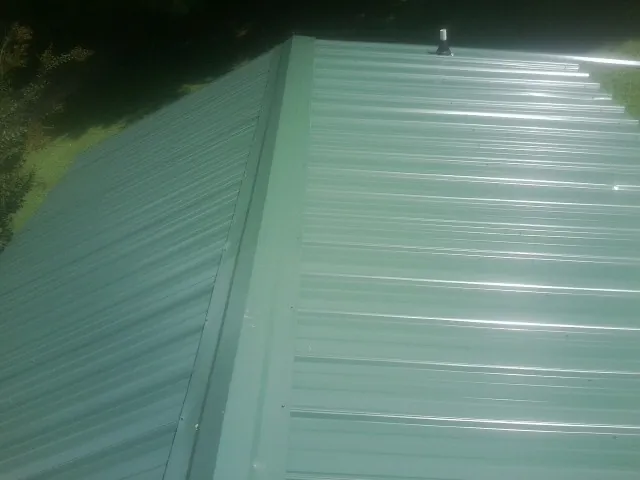 New green metal panels meeting at the ridge of a roof — Flat Roof Repair work by our crew in Aubrey