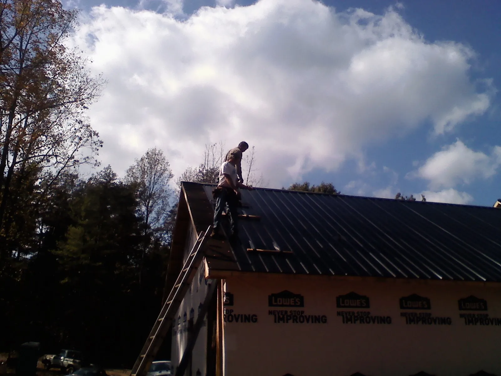 Roofer fastening dark metal panels high against a cloudy sky, from a Roof Inspection job in Aubrey