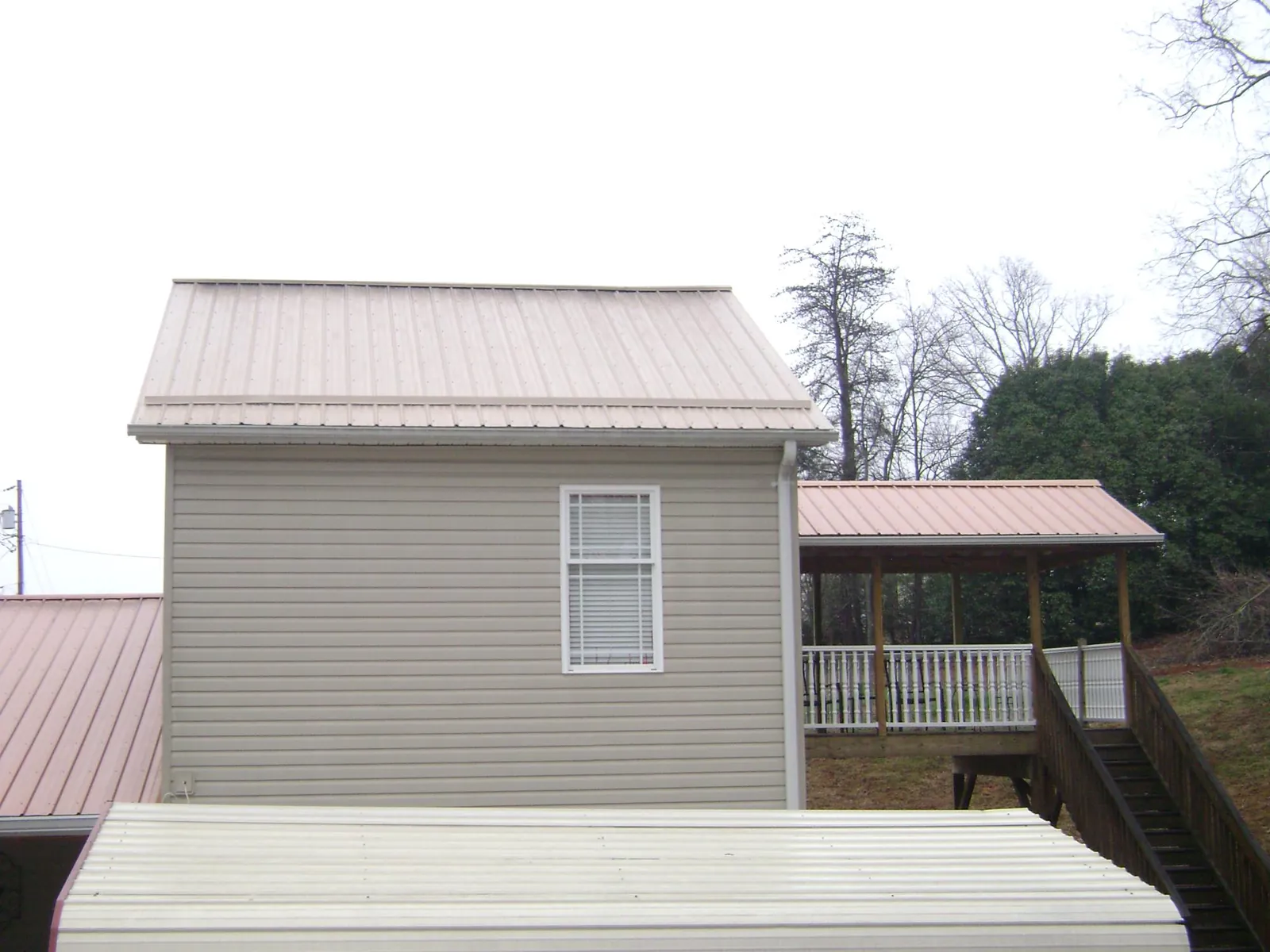 Tan metal roofs on a two story addition and attached porch, from a Roof Replacement job in Aubrey